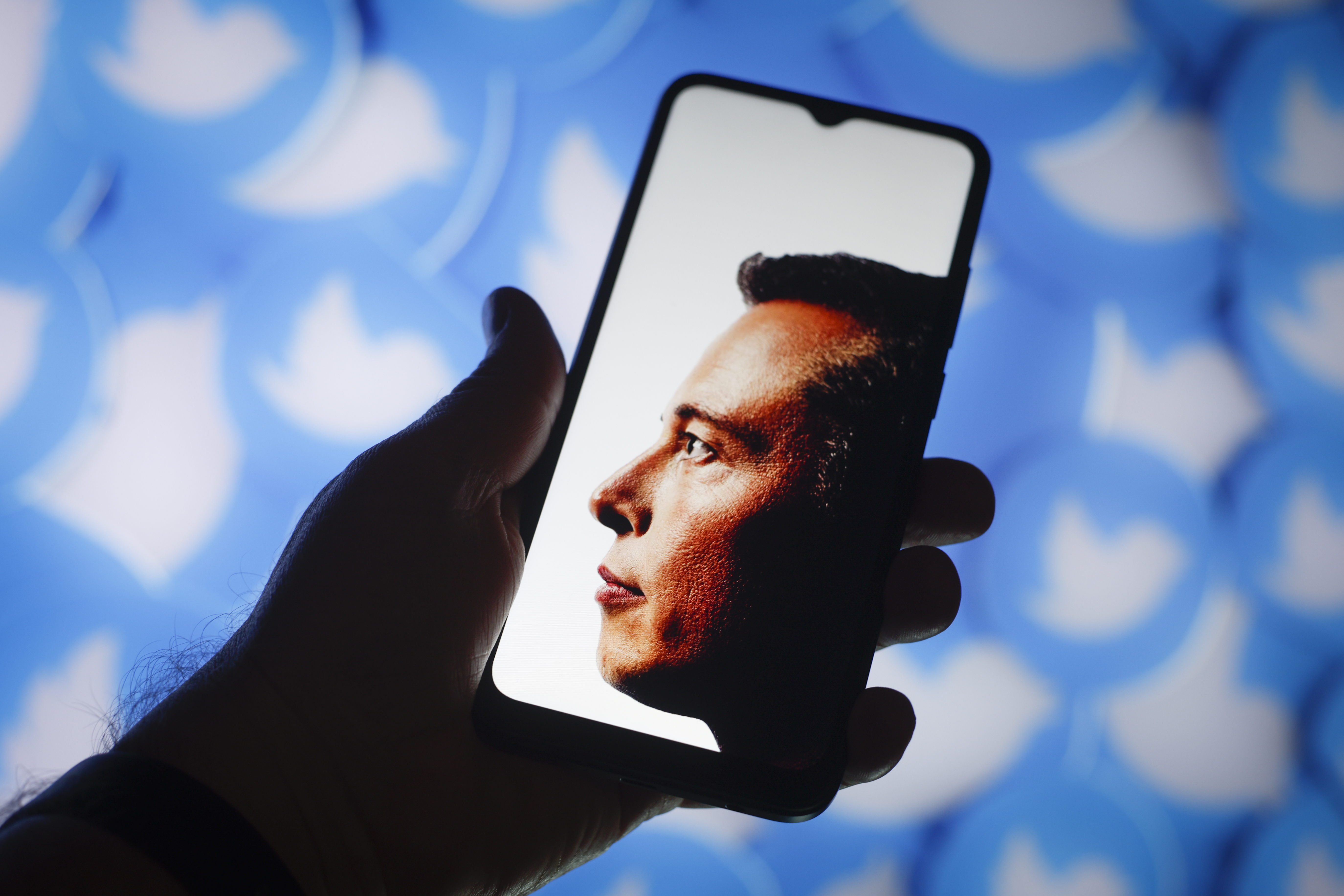 Фото Елон Маск по телефону з логотипами Twitter на фоновому режимі