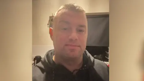 Джон Реддок Джон Реддок, дивлячись прямо в камеру. Він стояв на кухні і носить чорний джемпер.