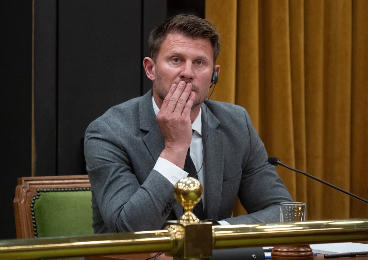 Чоловік потирає підборіддя, коли він сидить за столом мікрофоном.