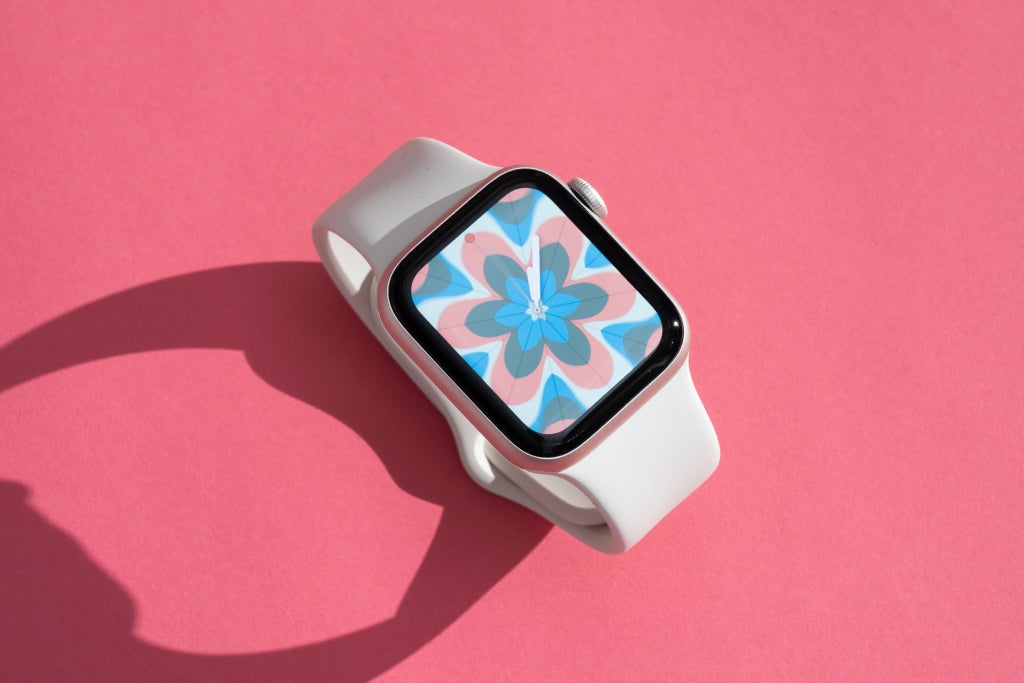 Apple Watch SE із фоном із геометричним малюнком на рожевій поверхні.